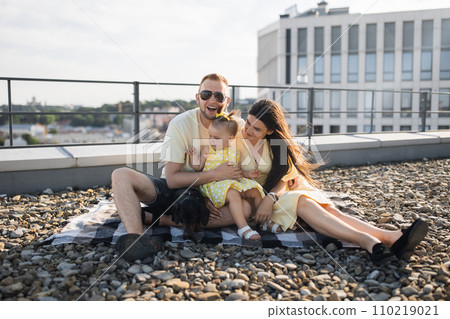 Joyful spouses having fun with daughter and dog on roof Joyful spouses having fun with daughter and dog on roof 110219021