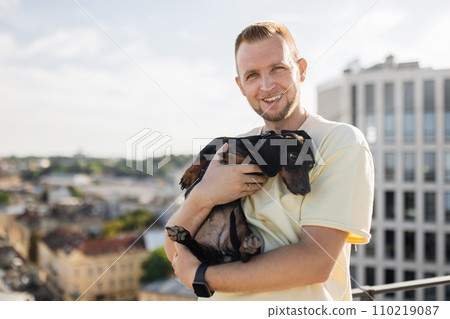 Positive man embracing his small black dog on rooftop 110219087