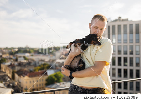 Positive man embracing his small black dog on rooftop 110219089