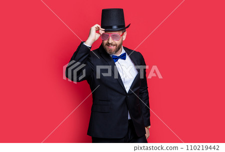 cheerful magician man wearing cylinder hat. man magician isolated on red background. cheerful magician man wearing cylinder hat. man magician isolated on red background. 110219442