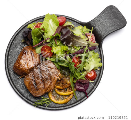 pieces of Organic grilled Tuna Steak on black ceramic serving dish with salad isolated 110219851