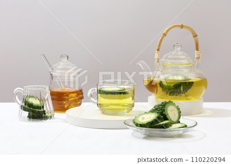 Tea set and glassware arranged on a white background with fresh bitter melon. Medical space with natural ingredients good for health. Front view. Tea set and glassware arranged on a white background with fresh bitter melon. Medical space with natural ingredients good for health. Front view. 110220294