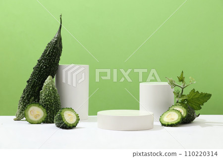 Three white cylindrical platforms of different sizes are displayed alongside fresh bitter melon on a minimalist background. Use bitter melon to effectively treat acne. Three white cylindrical platforms of different sizes are displayed alongside fresh bitter melon on a minimalist background. Use bitter melon to effectively treat acne. 110220314