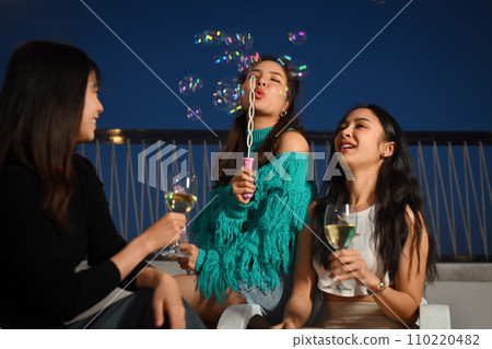 Group of young people having fun at outdoor rooftop party with drinks and blowing soap bubbles. Group of young people having fun at outdoor rooftop party with drinks and blowing soap bubbles. 110220482