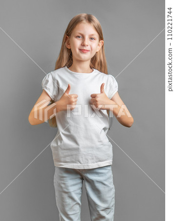 Happy child, little girl showing thumbs up gesture in a white T-shirt 110221744