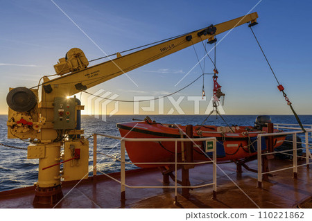 Orange rescue boat on big cargo vessel and crane. Man over board drill. Lifeboat training. Orange rescue boat on big cargo vessel and crane. Man over board drill. Lifeboat training. 110221862