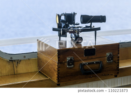 Nautical black sextant placed on wooden box in navigational bridge. Navigational equipment. Celestial navigation. 110221873