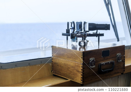 Nautical black sextant placed on wooden box in navigational bridge. Navigational equipment. Celestial navigation. 110221880