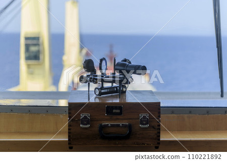 Nautical black sextant placed on wooden box in navigational bridge. Navigational equipment. Celestial navigation. 110221892