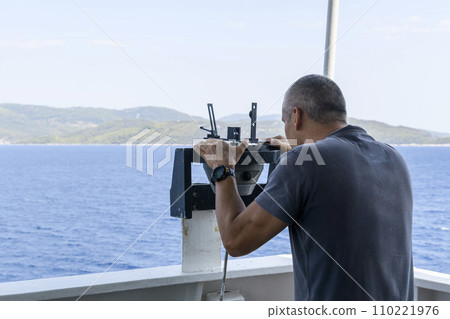 Navigational officer taking bearing with azimuth ring on gyro compass on the wing of navigational bridge. Navigational equipment usage. Observations. Navigational officer taking bearing with azimuth ring on gyro compass on the wing of navigational bridge. Navigational equipment usage. Observations. 110221976