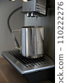Coffee machine flushes hot water into a silver milk jug 110222276