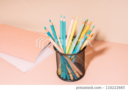 Colored pencils in a black glass with a notepad against a beige background Colored pencils in a black glass with a notepad against a beige background 110222665