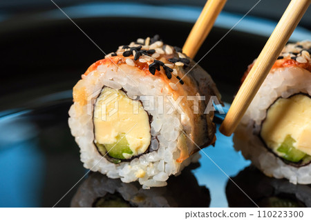 Close-up of sushi rolls with chopsticks on dark background 110223300
