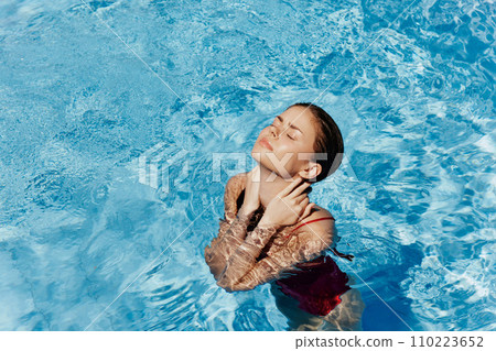 Happy woman swimming in pool in red swimsuit with loose long hair, skin protection with sunscreen, concept of relaxing on vacation. 110223652
