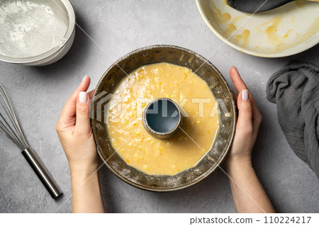 Cooking orange bundt cake. Top view, female hands holding raw, uncooked orange bundt cake. 110224217