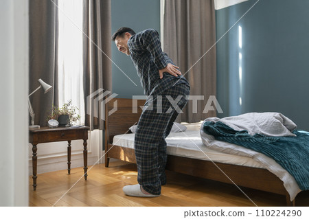 A middle-aged man in pajamas putting his hands on his hips next to the bed A middle-aged man in pajamas putting his hands on his hips next to the bed 110224290