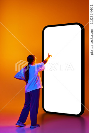 Back view photo of smart girl, student dressed in casual outfit pointing to huge smartphone with blank screen isolated gradient background. 110224461