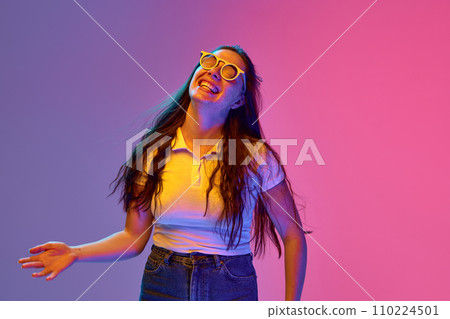 Portrait of positive, charming young brunette woman in sunglasses smiling an laughing against gradient background in neon light. Concept of emotions. Portrait of positive, charming young brunette woman in sunglasses smiling an laughing against gradient background in neon light. Concept of emotions. 110224501