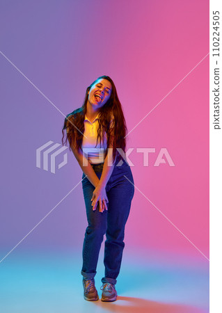 Full-length portrait of positive and funny young brunette woman with freckles grimacing against gradient background in neon light. Concept of emotions. 110224505