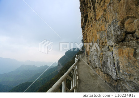 The trail on the mountain wall is surrounded by clouds and mist in the distance. 110224912