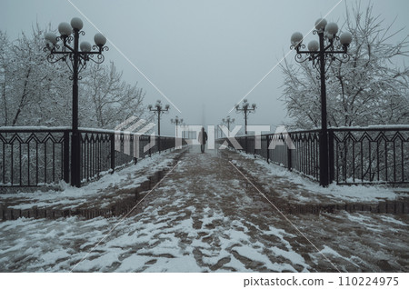 silhouette back man maniac walks on foggy bridge with lanterns in winter with snow and fog silhouette back man maniac walks on foggy bridge with lanterns in winter with snow and fog 110224975
