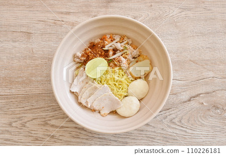 dry spicy tom yum Chinese yellow egg noodles with slice pork and ball couple fish line topping lemon on bowl dry spicy tom yum Chinese yellow egg noodles with slice pork and ball couple fish line topping lemon on bowl 110226181