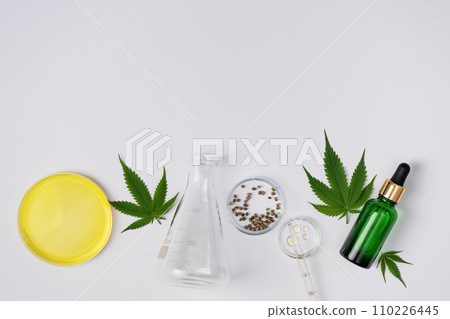 Cannabis CBD oil and hemp leaves with laboratory glass top view. Laboratory glassware and cannabis sativa herb and hemp seeds. Cannabis herbal alternative medicine. 110226445