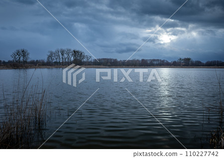 Dark evening clouds with glow from the moon over a calm lake Dark evening clouds with glow from the moon over a calm lake 110227742