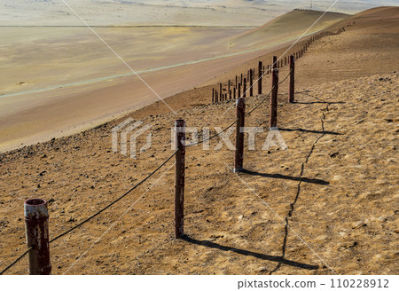 Stunning desert view in Paracas National Reserve with rusty metal fence delimiting the protected area, Peru  110228912