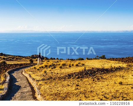 Stunning view of lake Titicaca at sunset, with a local farmer riding down to the village through a stone path, Amantani island, Peru  110228916