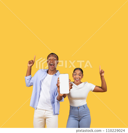 Ecstatic black couple pointing upwards, showcasing smartphone, banner 110229024