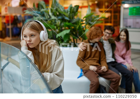 Little girl feeling upset to be ignoring with older friends, in shopping mall Little girl feeling upset to be ignoring with older friends, in shopping mall 110229350