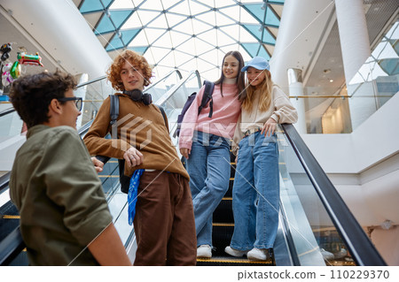 Happy teenage friends team moving staircase at shopping mall Happy teenage friends team moving staircase at shopping mall 110229370
