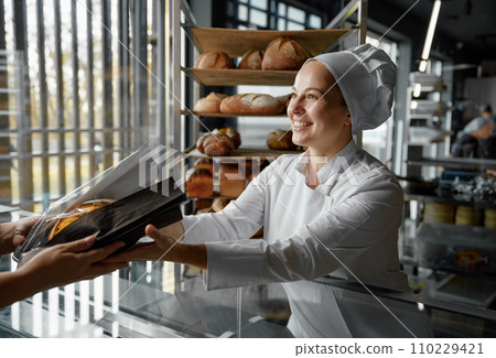 Friendly smiling saleswoman in bakery passing bread over counter desk 110229421