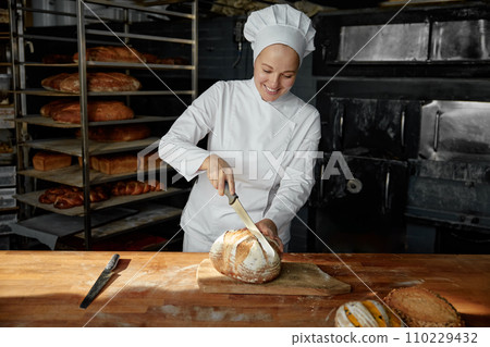 Woman chef cutting healthy bread on wooden board at bakehouse kitchen 110229432