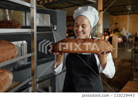 Smiling female baker smells freshly baked bread Smiling female baker smells freshly baked bread 110229443