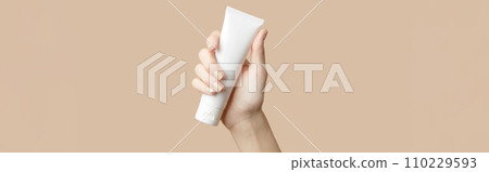 A womans hand holding a white cosmetic tube on a beige background. Care products A womans hand holding a white cosmetic tube on a beige background. Care products 110229593