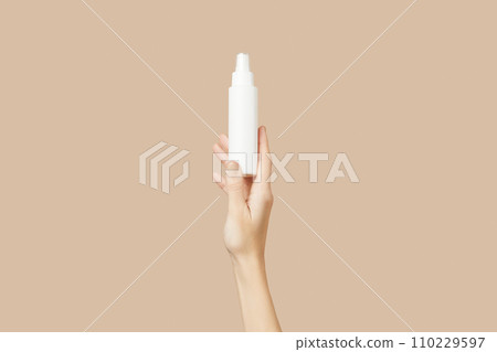 A womans hand holding a white cosmetic bottle on a beige background. Beauty treatment concept A womans hand holding a white cosmetic bottle on a beige background. Beauty treatment concept 110229597
