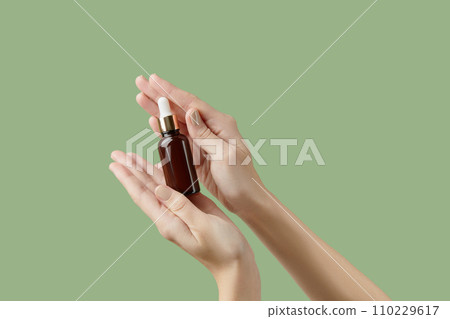A womans hands holding a brown bottle of serum on a green background A womans hands holding a brown bottle of serum on a green background 110229617