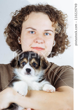 Close-up portrait of face of charming woman, owner of small Welsh corgi puppy, whom she holds in her arms. Dog food. 110229749