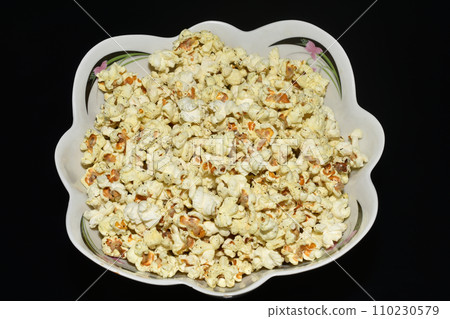 Delicious popcorn lies in a plate on a dark background. 110230579