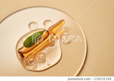 Ampoule in a drop of cosmetic gel on a beige background. Ampoule in a drop of cosmetic gel on a beige background. 110231149