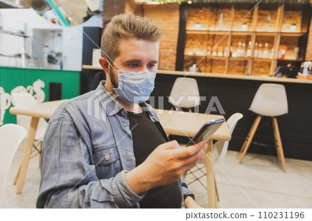 Man wears medical face mask in public area and using smartphone to do work business and social network communication in public cafe work space area. Man wears medical face mask in public area and using smartphone to do work business and social network communication in public cafe work space area. 110231196