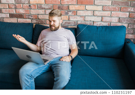 Millennial man at home on couch talking by video call with a laptop. Technologies for freelancer and communication online concept Millennial man at home on couch talking by video call with a laptop. Technologies for freelancer and communication online concept 110231197