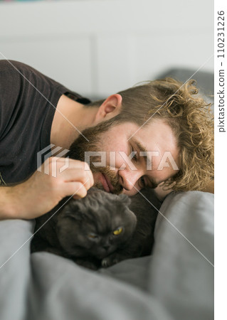 Funny scottish fold cat lying with male owner in bed. Pet concept 110231226
