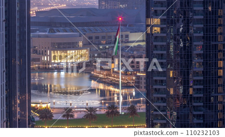 Aerial view of Dubai Fountain in downtown with palms in park next to shopping mall and souq night to day timelapse, UAE 110232103