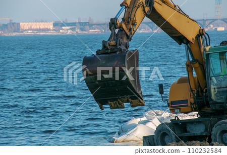 Excavator works to strengthen the embankment. Hydraulic excavator working on the river bank Excavator works to strengthen the embankment. Hydraulic excavator working on the river bank 110232584