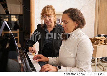Young adult Asian female pianist, music teacher teaching piano and music lesson to a woman Young adult Asian female pianist, music teacher teaching piano and music lesson to a woman 110233350