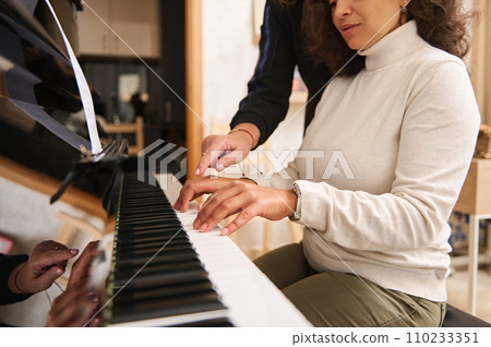 Close-up portrait of a pretty woman learning playing grand piano with her teacher pianist musician during music class 110233351