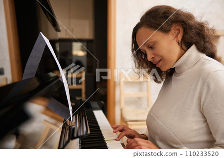 Authentic multiracial young woman pianist playing piano and singing song, creates music, practices on chord instrument 110233520